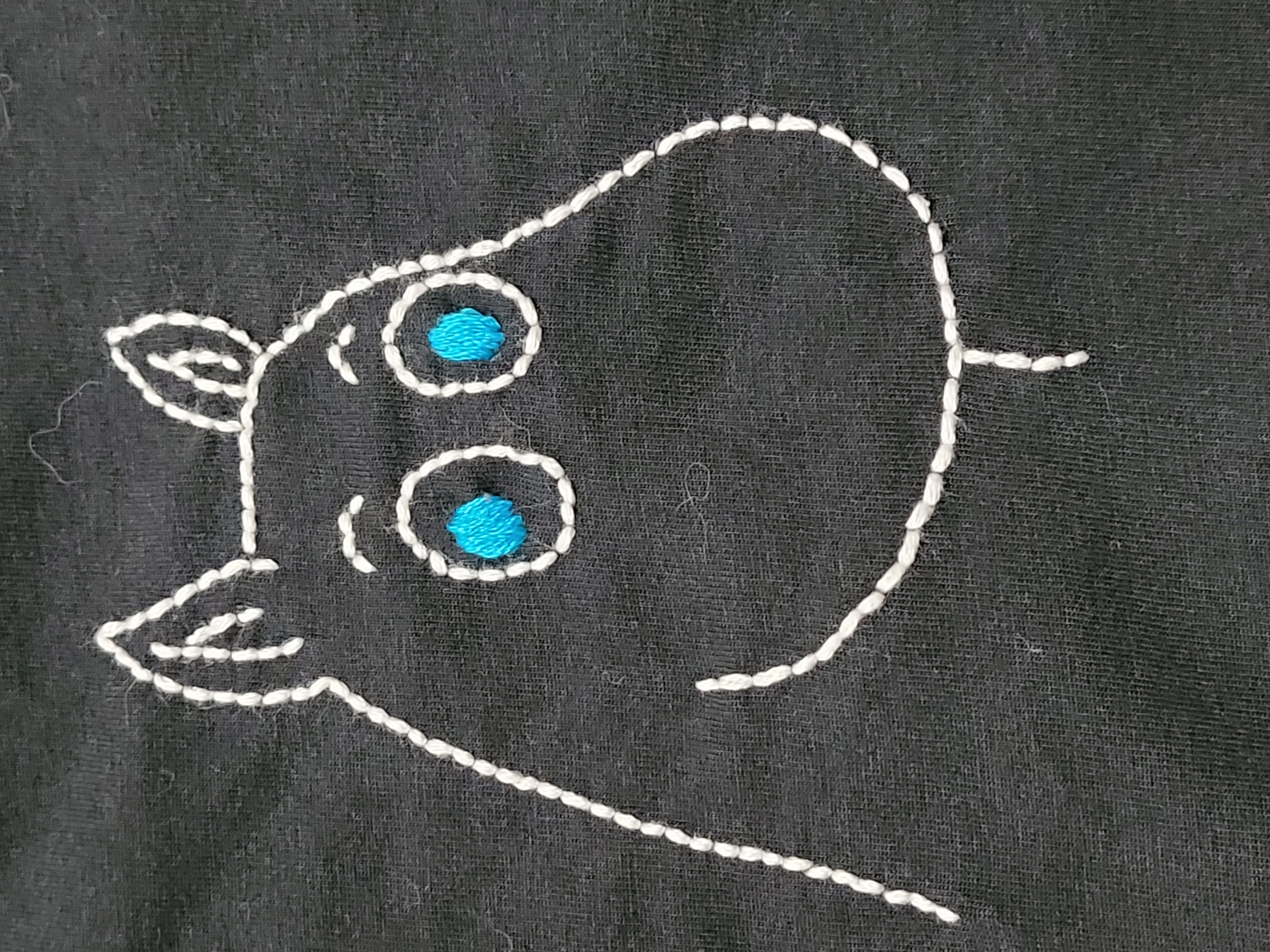 A close up picture of simple embroidery of the character Moomin on a T shirt.