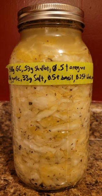A side picture of the ferment. The cabbage is becoming a greyish yellow and translucent, there are many air pockets, and the liquid has become entirely opaque.