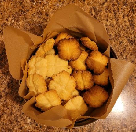 A paper-lined tin of shortbread cookies, each made in the shape of four-pointed stars. Half are burnt, half are golden brown.